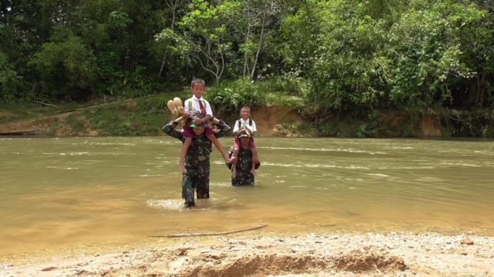 Prajurit TNI membantu menyeberangkan bocah SD agar bisa menyeberangi sungai menuju sekolah. Foto Dok Kodam XII/Tpr